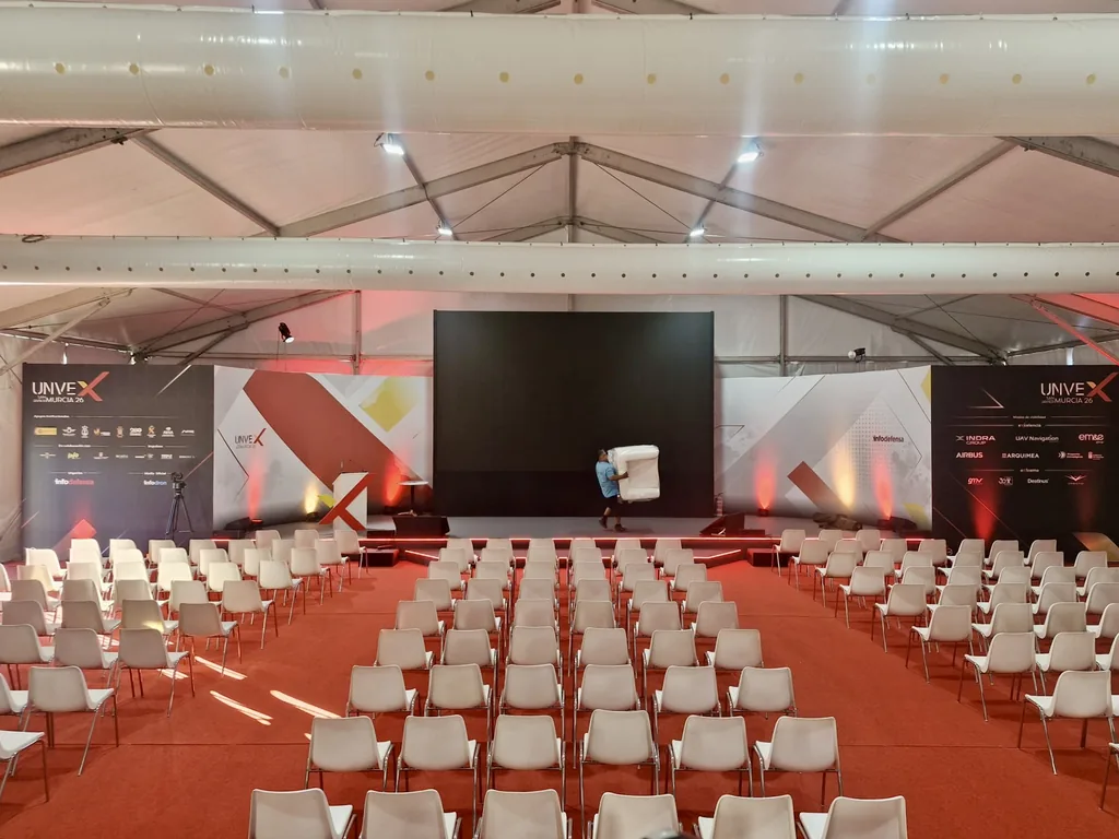Auditorio de UNVEX 2026 con escenario, pantalla y sillas blancas bajo carpa