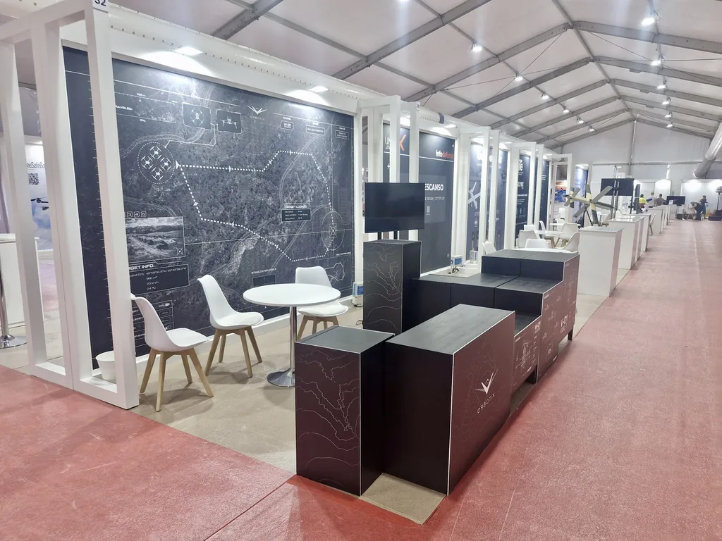 Stand de expositor en la carpa de UNVEX 2026 con mobiliario negro y gráfica de mapa